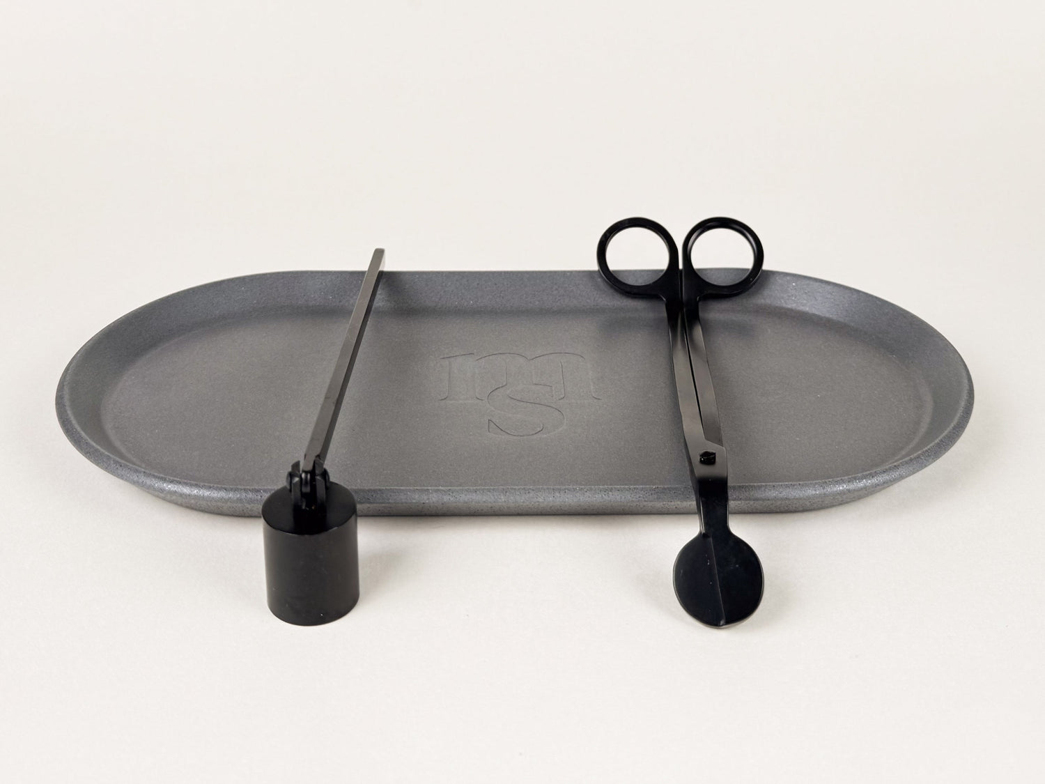 Photograph of a grey coloured jesmonite tray with a black candle snuffer and wick trimmer against an off-white background