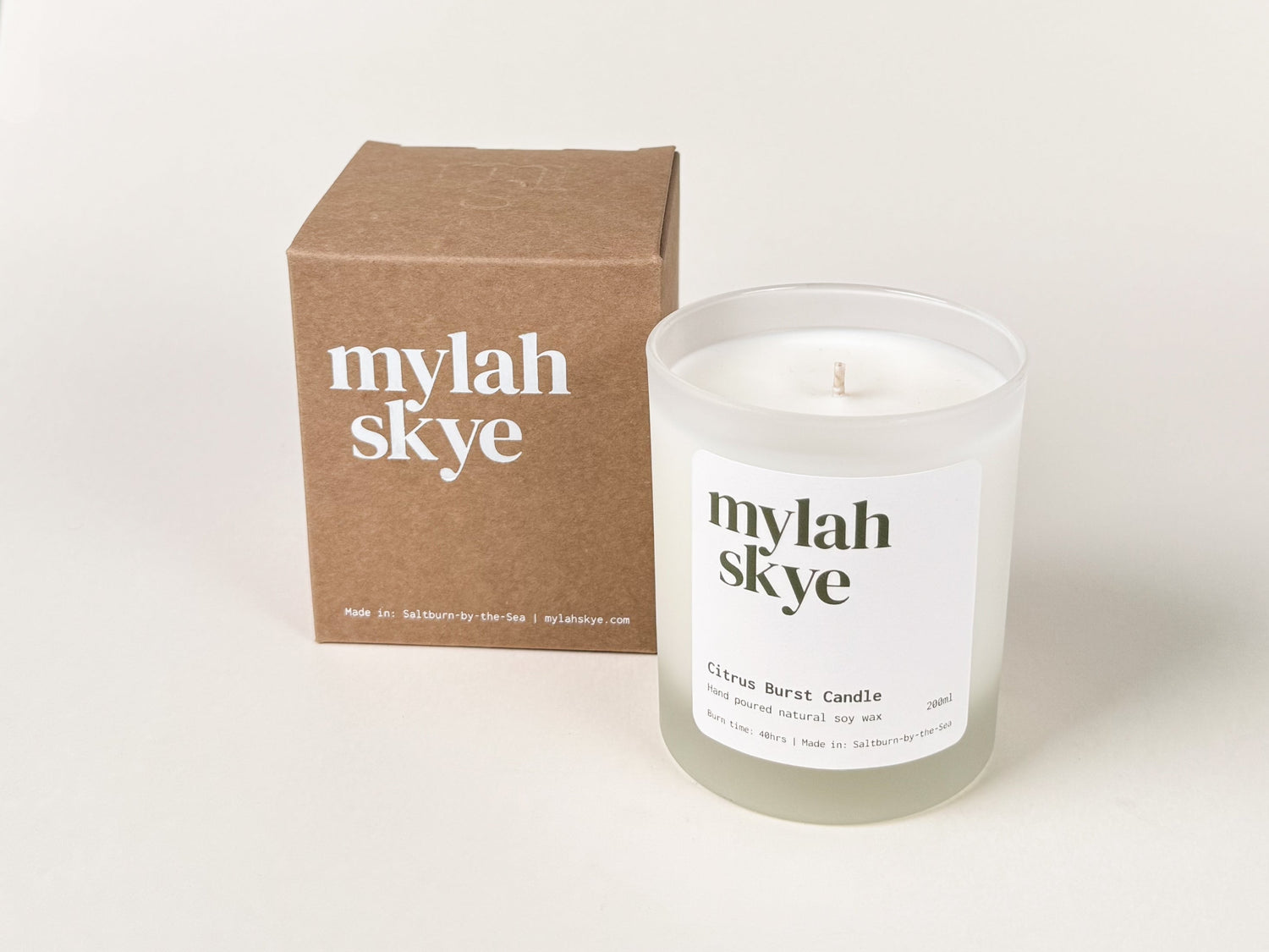 Photograph of a frosted glass candle jar and a kraft brown cardboard packaging box against an off-white background