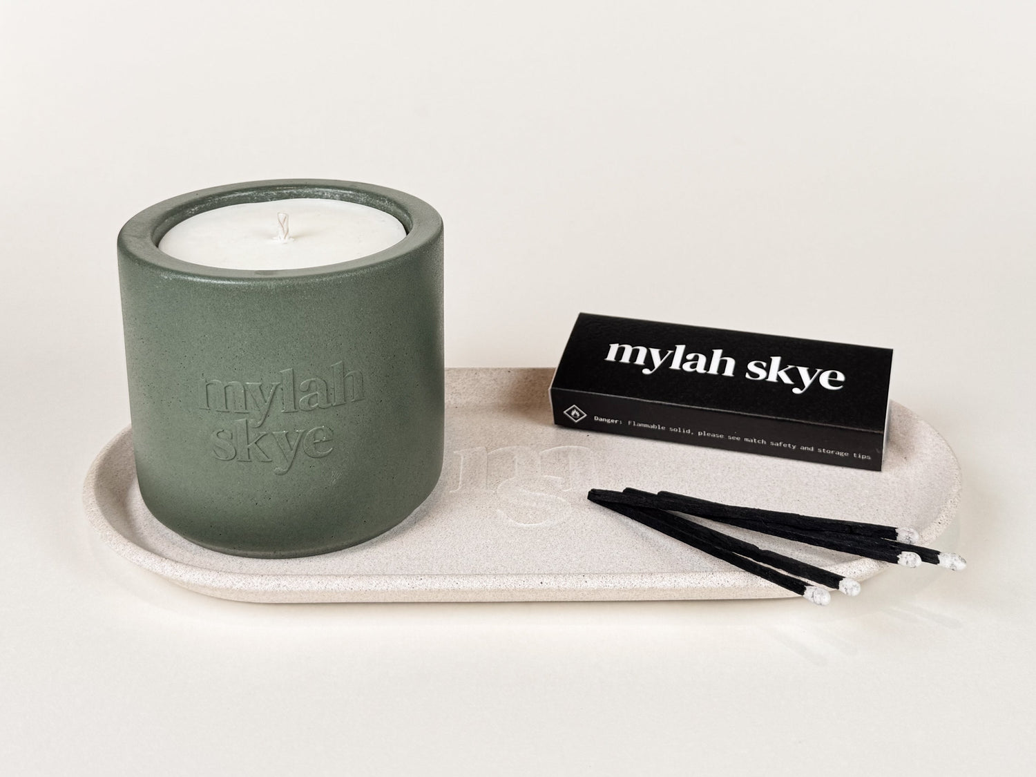 Photograph of a green jesmonite pot and black matches on a beige jesmonite tray against an off white background